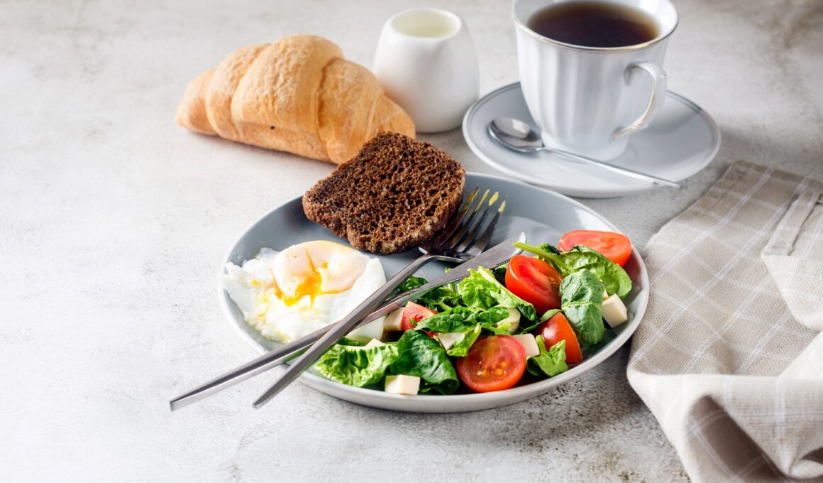 Salad in plate, egg, cup of coffee and croissant , fresh tulips in vase on clean white